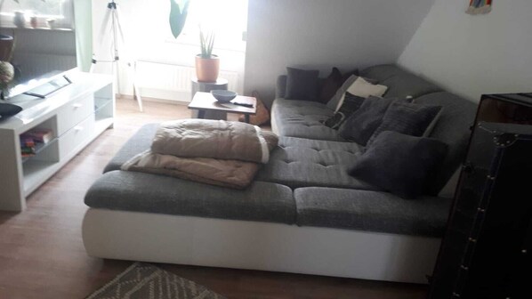 Un salon chaleureux avec un canapé gris, une petite table d’appoint et une plante en pot.
