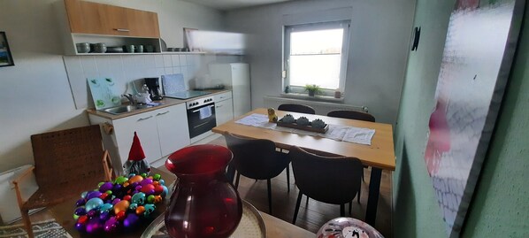 A compact kitchen with a dining area, including a table with chairs, a red vase, and colorful ornaments.