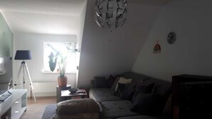 A living room with a sofa, a lamp, a tripod, and a potted plant. - Apartment in a central location (06502 Thale OT Westerhausen)
