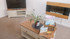 Una habitación con televisión sobre un mueble bajo, una mesa de centro de madera con una planta, una revista y un libro de visitas.