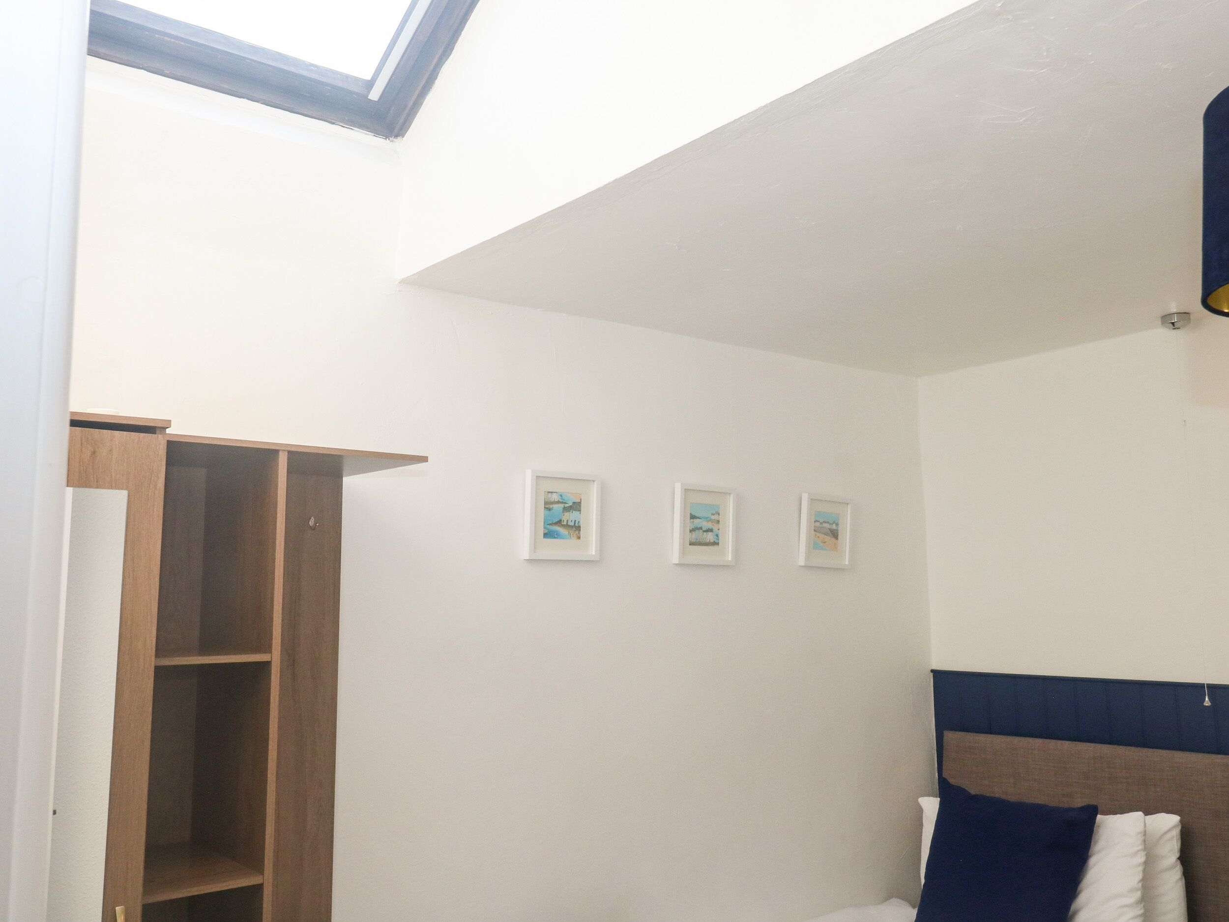 A bedroom with a skylight, a wooden wardrobe, and three framed pictures on the wall.