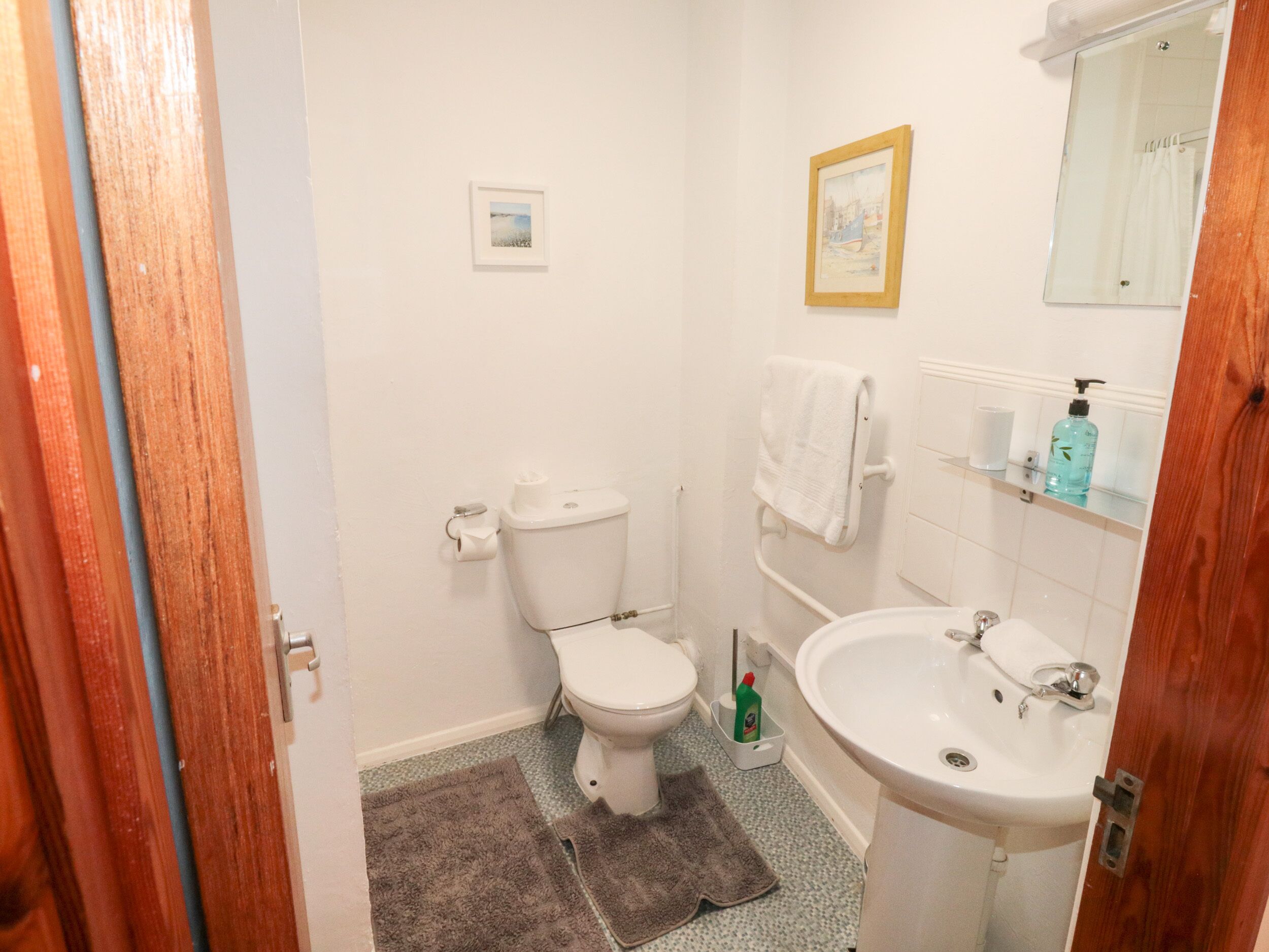 A small, clean bathroom with a toilet, sink, and a mirror. There are two framed pictures on the wall.