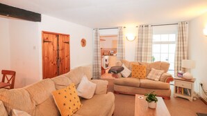 A cozy living room with two sofas, a wooden door, a small table with a plant, and a lamp. - Primrose Cottage (Paignton)