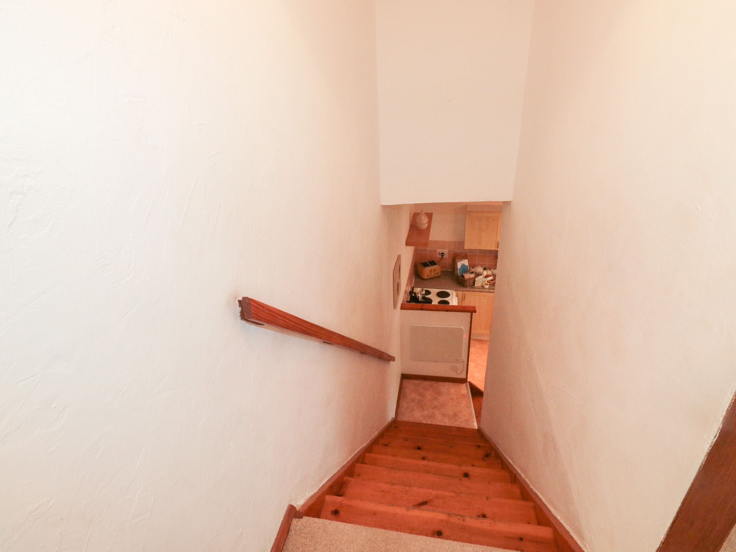A narrow staircase leading to a kitchen area with a wooden handrail and a small countertop.