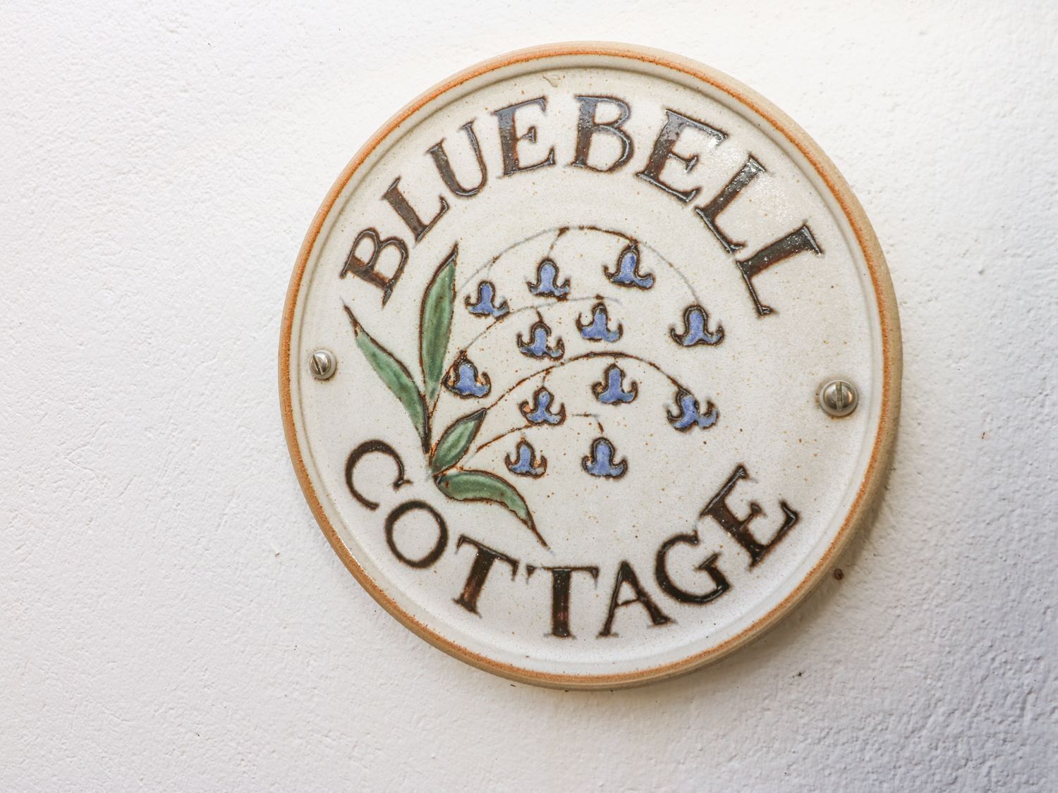 Un panneau circulaire portant l’inscription « BLUEBELI COTTAGE » et agrémenté d’éléments décoratifs, notamment des feuilles et des fleurs.