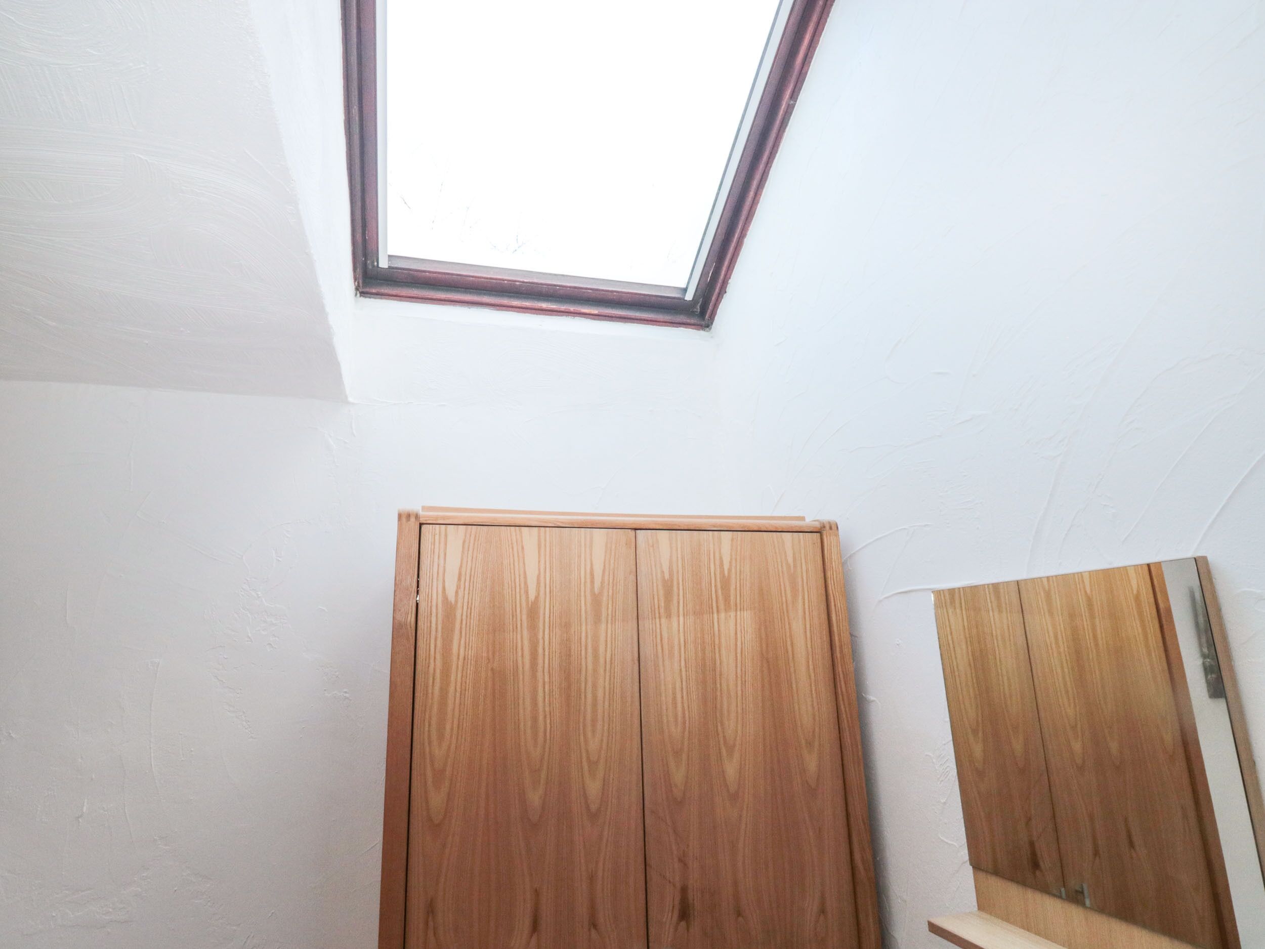 A room with a skylight, wooden wardrobe, and a mirror.