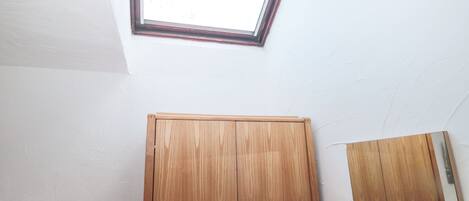A room with a skylight, wooden wardrobe, and a mirror.