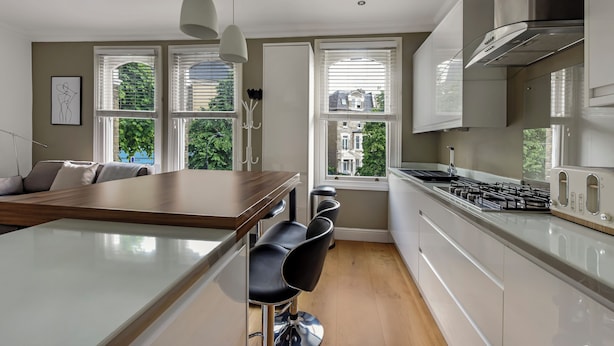 A modern kitchen with a central island, bar stools, and a view of greenery outside. - Immaculate 2 Bed Flat in West Kensington (London)