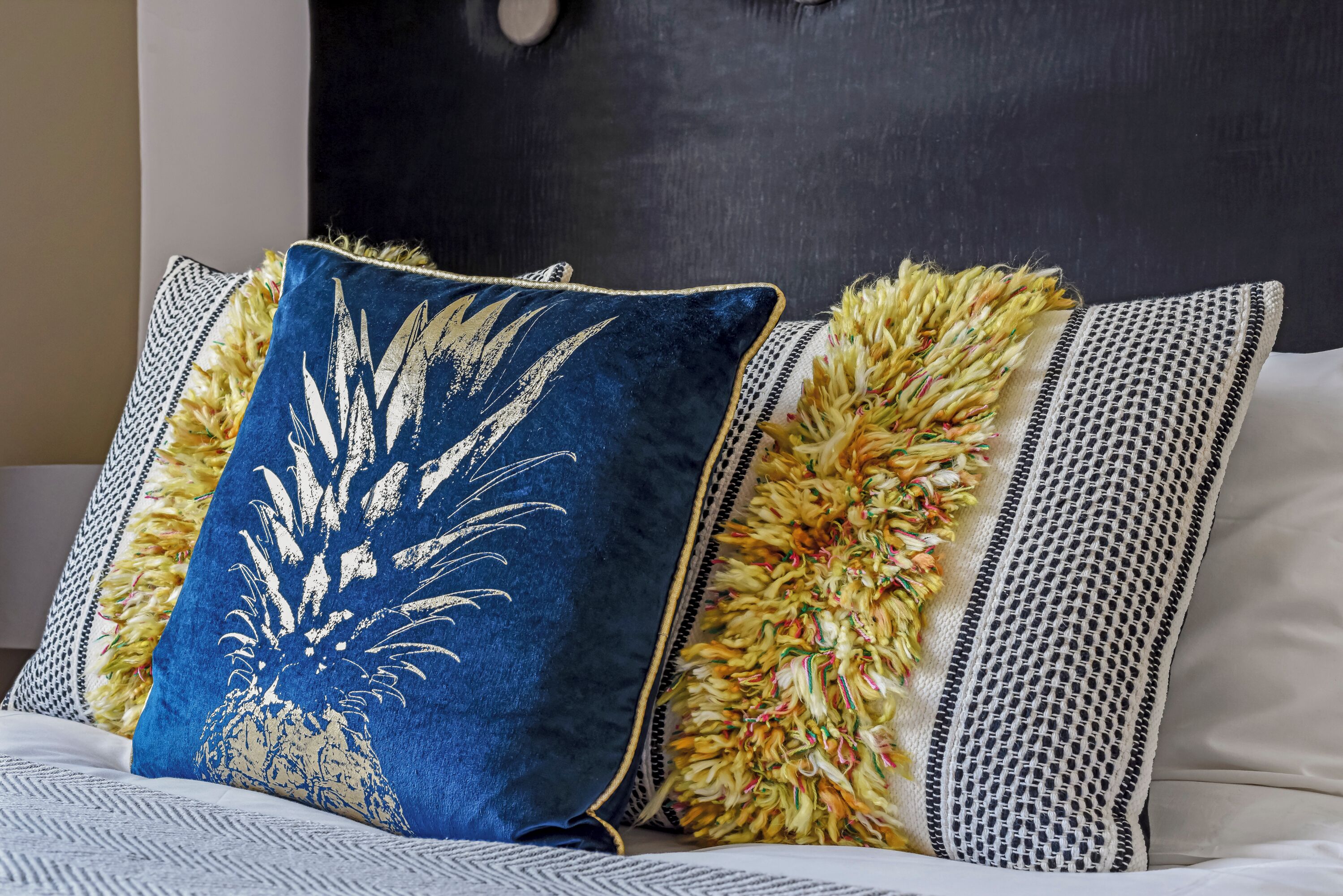 A bed with a blue pillow featuring a white palm tree design and a textured pillow with a yellow and white fringe.