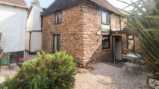 A stone building with a sloped roof, a small porch, and a gravel driveway.