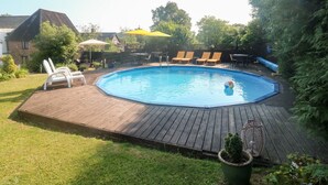 A backyard with a swimming pool, wooden deck, and outdoor furniture.
