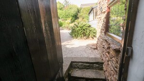 A doorway leading to a gravel path with a stone wall and a window.