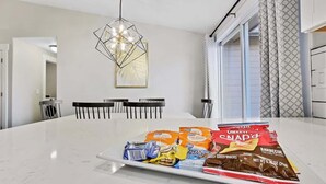 A modern kitchen with a marble countertop, a geometric pendant light, and a dining area with a white table and chairs. - Calming 3 bedroom home with designer details in Na (Nampa)