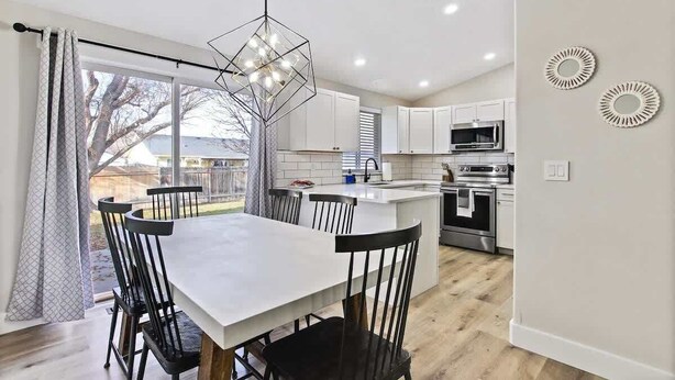 A modern kitchen with white cabinets, a central island, and a dining area with a white table and black chairs. - Calming 3 bedroom home with designer details in Na (Nampa)
