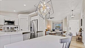 A modern kitchen with white cabinetry, a central island, and a dining area with a large table and chairs. - Calming 3 bedroom home with designer details in Na (Nampa)