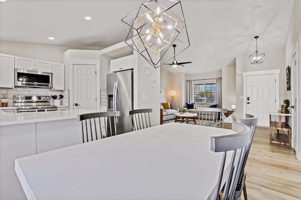 A modern kitchen with white cabinetry, a central island, and a dining area with a large table and chairs. - Calming 3 bedroom home with designer details in Na (Nampa)