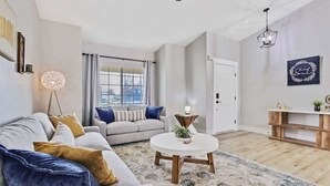 A living room with a sofa, a round coffee table, a floor lamp, and a wooden console table with decorative items. - Calming 3 bedroom home with designer details in Na (Nampa)