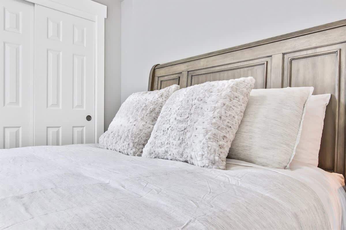 Cama com cabeceira de madeira, roupa de cama branca e dois travesseiros.