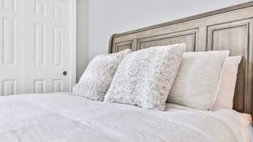 Cama com cabeceira de madeira, roupa de cama branca e dois travesseiros.