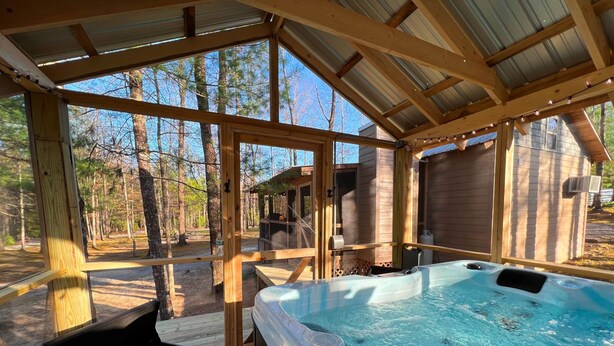 Eine Holzterrasse mit Whirlpool, Holzliegen und Blick auf den umliegenden Wald.