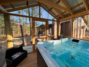 En træterrasse med jacuzzi, træliggestole og udsigt til den omkringliggende skov.