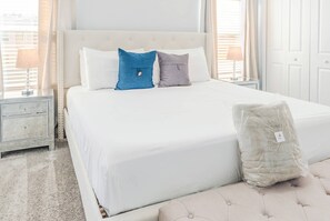 A neatly made bed with white bedding, two pillows, a bedside table with a lamp, and a bag of linens on the floor. - Spacious 4BR Pool Home Near Disney - Storey Lake (Kissimmee)