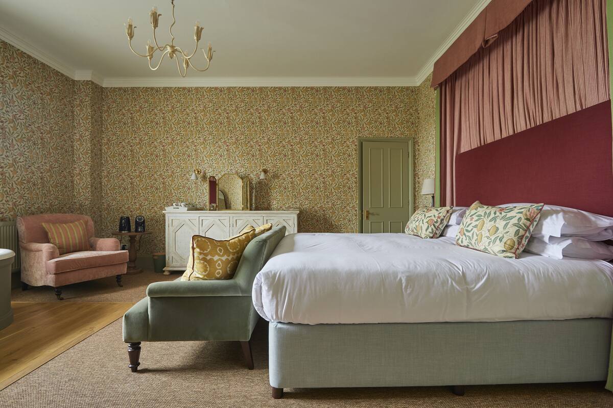 A bedroom with a large bed, two armchairs, a dresser, and a chandelier.