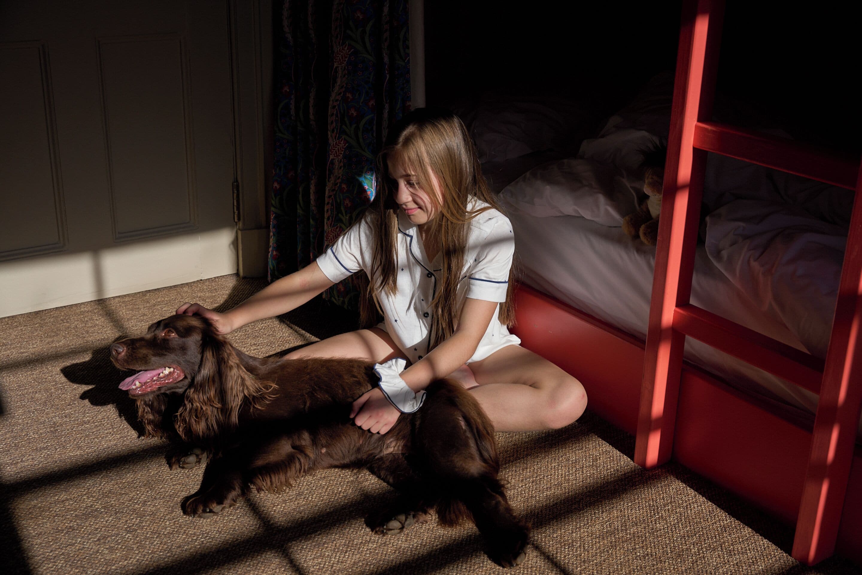 A person sitting on the floor next to a bed with a dog.