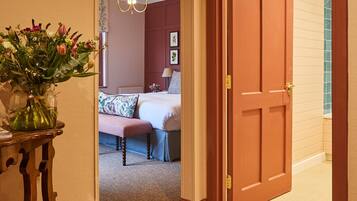 Un pasillo de hotel con una puerta de madera que da a un dormitorio con cama, mesita de noche y un jarrón de flores.