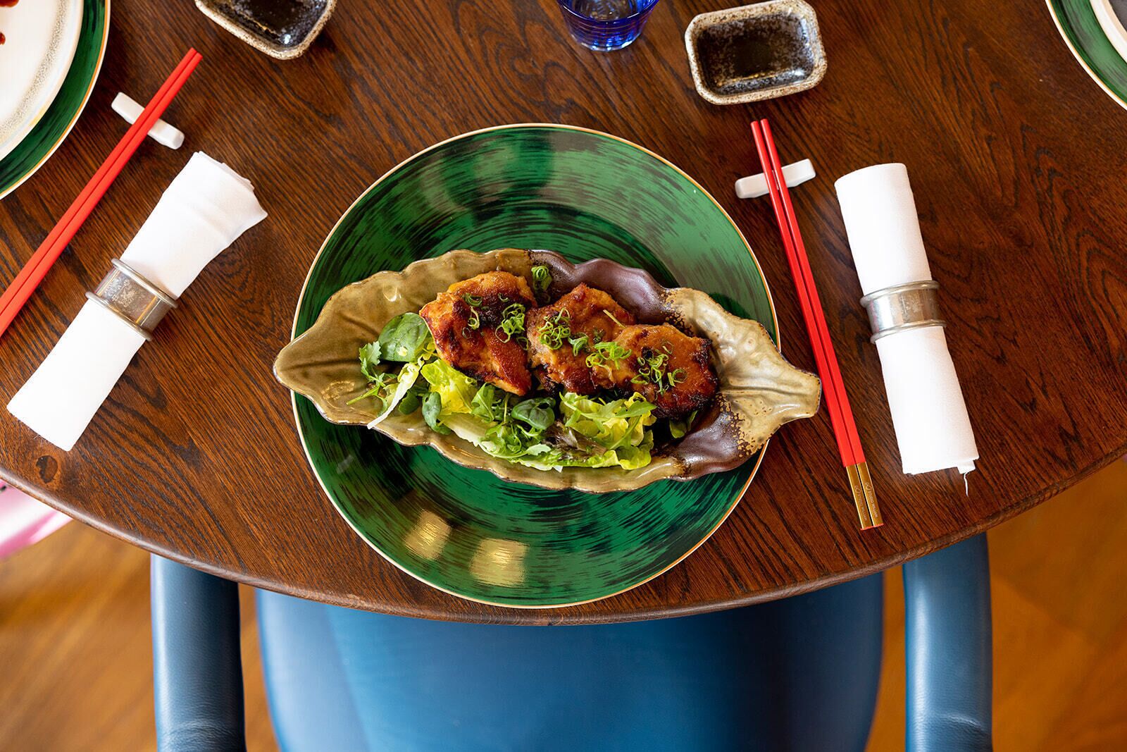 A table with a green plate containing food, chopsticks, and a small dish.
