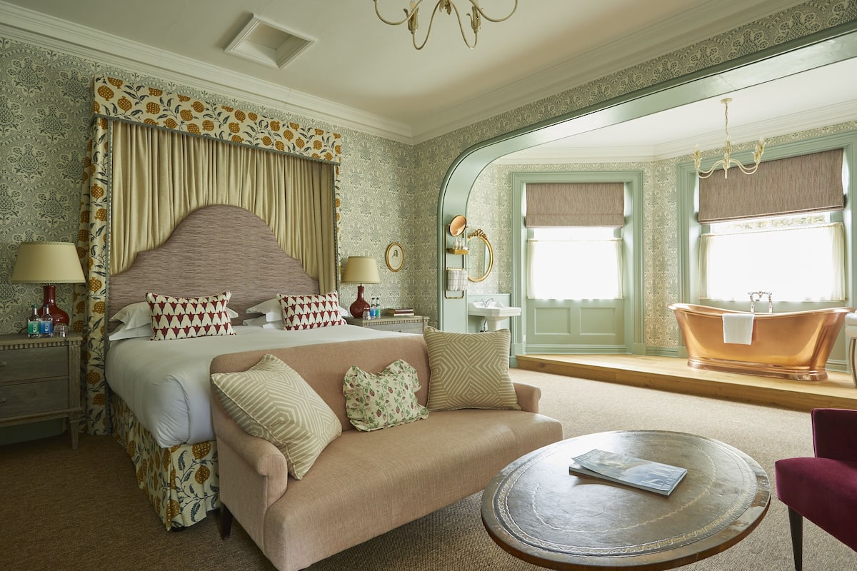 A bedroom with a large bed, a sofa, a round coffee table, and a bathtub in the corner.