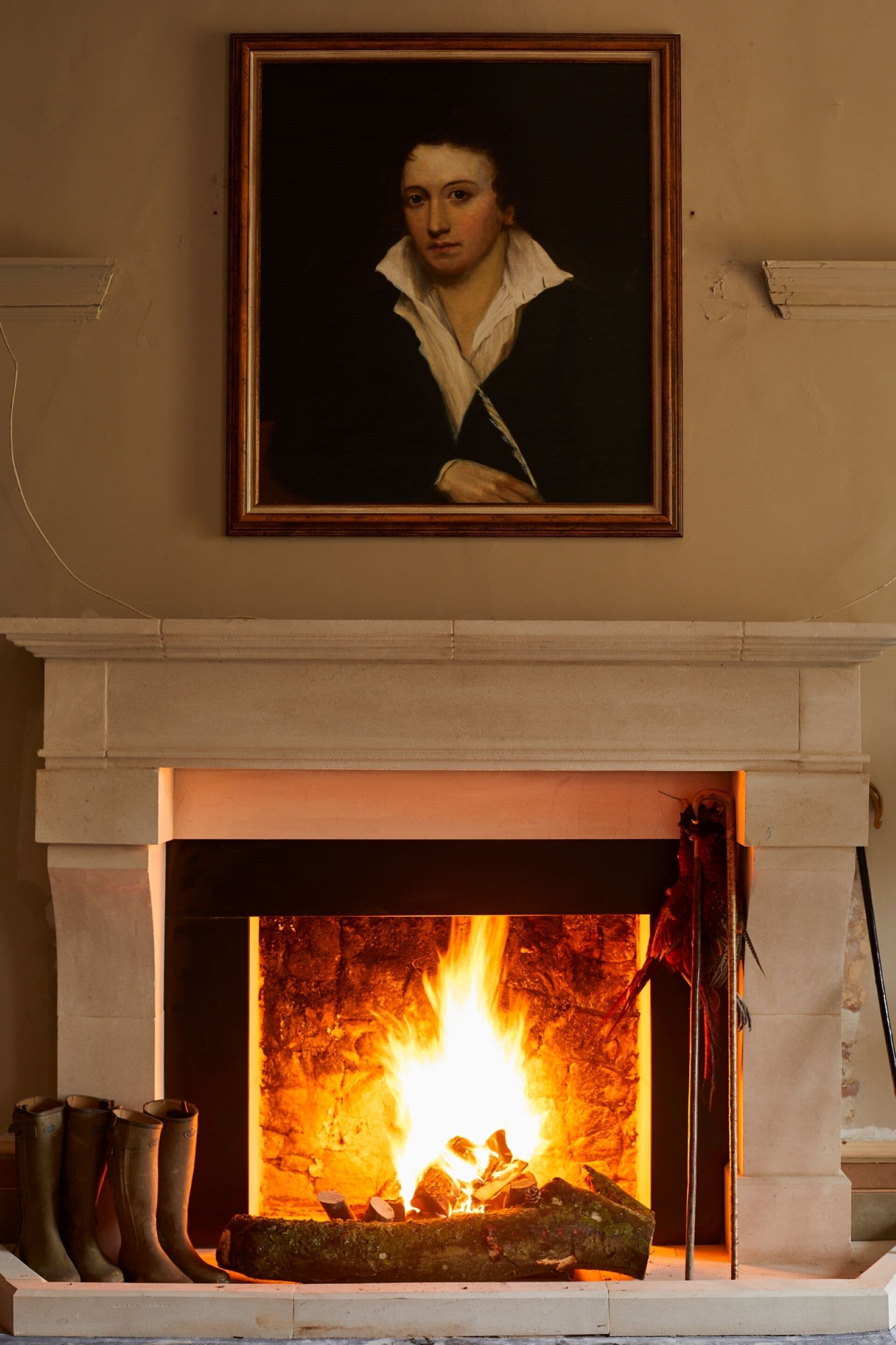 Una chimenea con un retrato sobre ella, una pared de piedra y un par de botas a un lado de la chimenea.