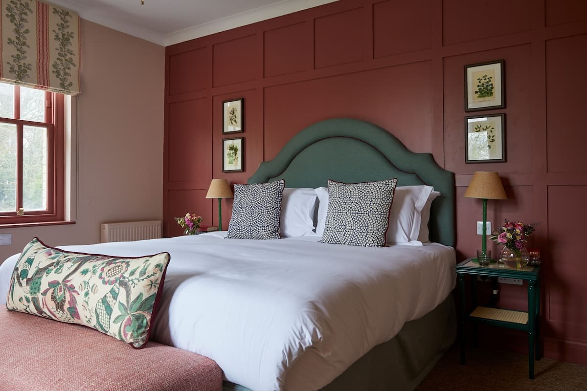 A bedroom with a large bed, two bedside tables, a window with curtains, and framed pictures on the wall.