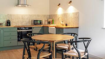 A compact kitchen with a round wooden table and four chairs, a microwave, a kettle, and a sink.