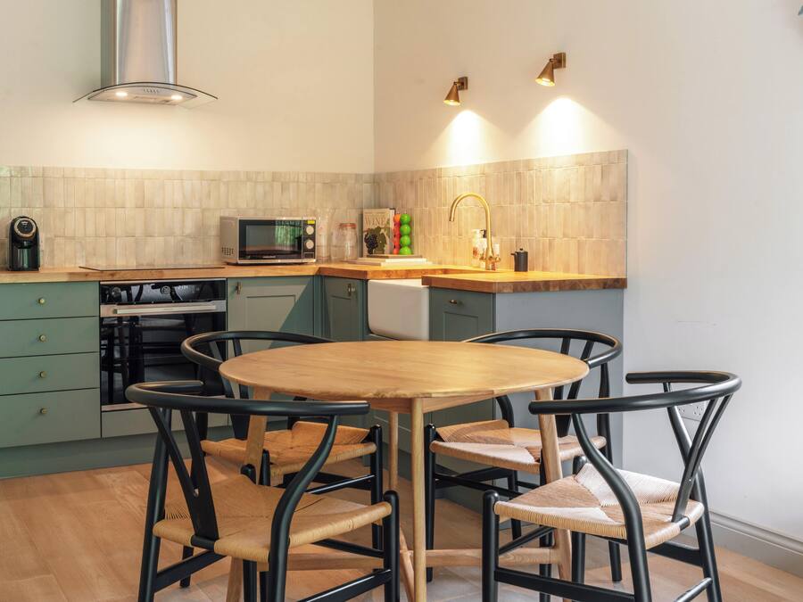 A compact kitchen with a round wooden table and four chairs, a microwave, a kettle, and a sink.