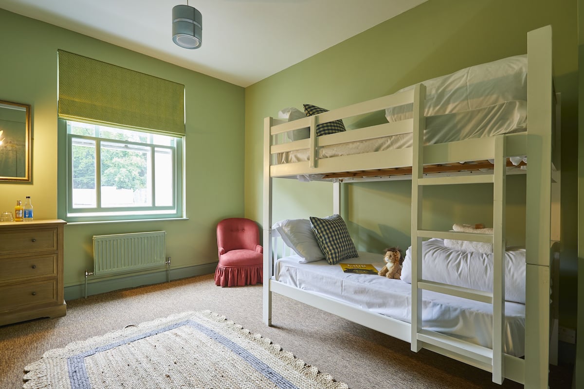 A bunk bed room with a window, a radiator, a chair, and a dresser.