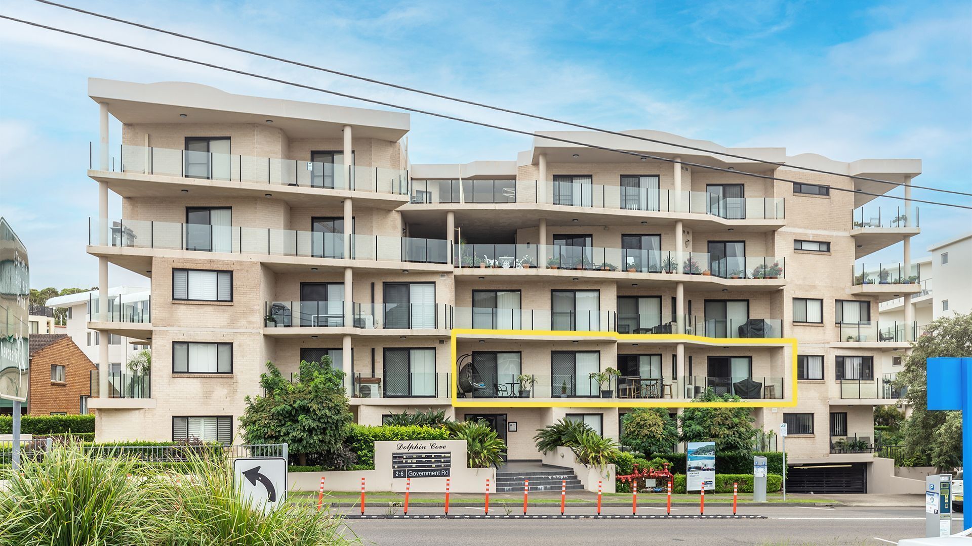 A multi-story residential building with balconies, a sign reading "Dolphin Cove," and a road sign indicating "2-6 Government Rd."