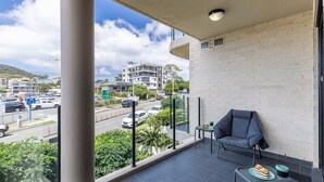 A balcony with a view of a busy street, a chair, and a small table with a cake. - Dolphin Cove 8, 2-6 Government Rd - Air conditioning, Wi-Fi, lift, secure parking and close to town (Nelson Bay)