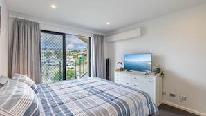 A bedroom with a bed, a TV, a dresser, and a balcony with a view of the city. - Dolphin Cove 8, 2-6 Government Rd - Air conditioning, Wi-Fi, lift, secure parking and close to town (Nelson Bay)
