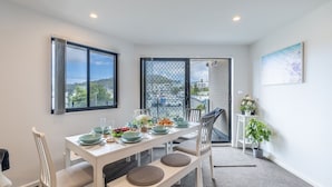 A modern dining area with a white table set for four, large windows, and a view of the city. - Dolphin Cove 8, 2-6 Government Rd - Air conditioning, Wi-Fi, lift, secure parking and close to town (Nelson Bay)