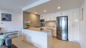 A modern kitchen with white cabinets, a stainless steel refrigerator, a microwave, and a tiled backsplash. - Dolphin Cove 8, 2-6 Government Rd - Air conditioning, Wi-Fi, lift, secure parking and close to town (Nelson Bay)