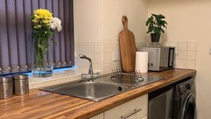 A modern kitchen with a stainless steel sink, wooden countertop, built-in oven, and a washing machine. - "the Old Forge"- 5 Minutes Away From Motorway (Bradford)