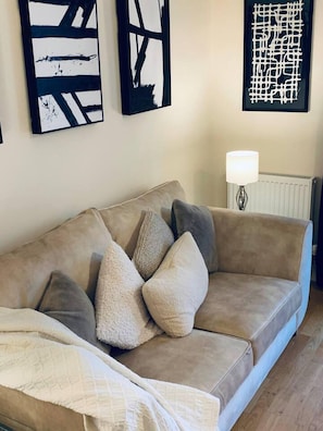 A beige sofa with multiple cushions, a white lamp, and abstract wall art.