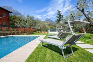 A poolside area with lounge chairs and a red building in the background. - Maison Bellini: near to the beach and with pool (Toscolano-Maderno)