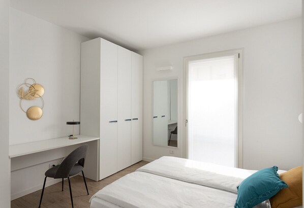 Un dormitorio con cama, escritorio, silla, armario y espejo.