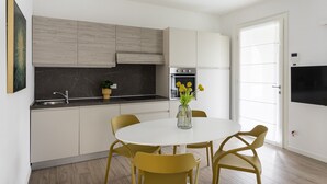 Eine moderne Küche mit Essbereich, ausgestattet mit einem runden Tisch und gelben Stühlen, einem eingebauten Backofen und einem großen Fenster.