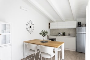 Une cuisine moderne avec des meubles blancs, une table à manger en bois et un réfrigérateur en acier inoxydable.