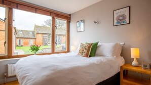 A bedroom with a large bed, a bedside table with a lamp, and a view of a brick building outside. - Granary at Rectory Farm - sleeps 5 guests  in 3 bedrooms (Shipston-on-Stour)