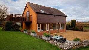 A two-story house with a balcony, a patio with a table and chairs, and a well-maintained garden. - Granary at Rectory Farm - sleeps 5 guests  in 3 bedrooms (Shipston-on-Stour)