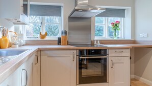 Een moderne keuken met een roestvrijstalen afzuigkap, een inbouwoven en een raam met uitzicht op bomen.